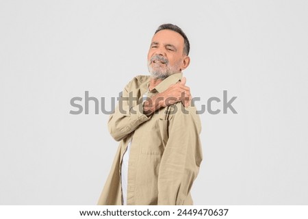 An old man touches his shoulder, showing a pained expression, isolated on a white background, got injured