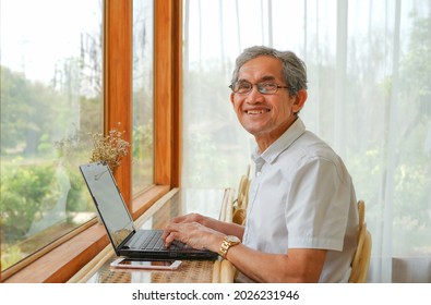 an old man using computer laptop and mobile phone put on beside him, inside the room at his garden house, concept lifestyle, quality of life, technology in elderly people.