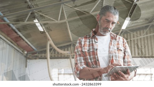 Old man using a tablet in a warehouse with stats and graphs.
