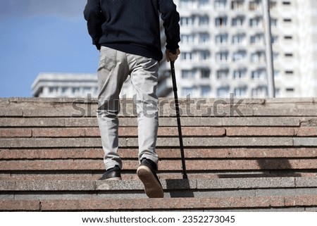 Old man with walking cane climbing stairs on city street. Concept for disability, limping adult