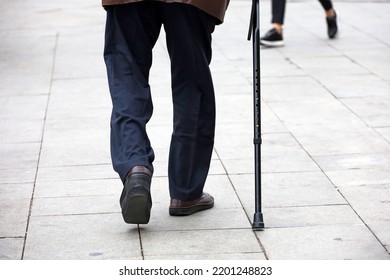 Old man walking with a cane down the city street. Diseases of the spine and legs of elderly people