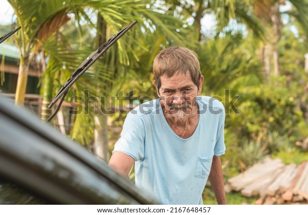 An old man washes\
his black hatchback. A car owner cleaning and taking care of his\
auto early in the morning.