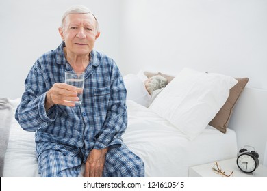 Old Man With A Water Glass Sitting On The Bed