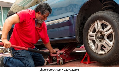 An Old Man Wearing A Red Shirt Changing The Tire Of His Truck At Home