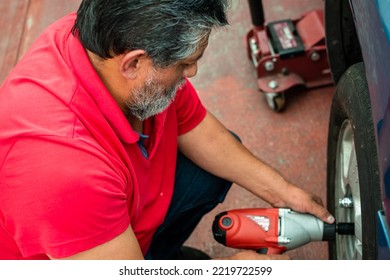 An Old Man Wearing A Red Shirt Changing The Tire Of His Truck At Home