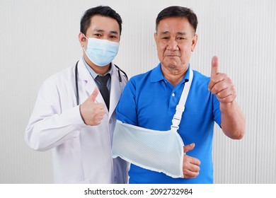 An Old Man Wears An Arm Support Due To A Broken Arm. And There Was A Doctor Standing Beside With Raising Fingers