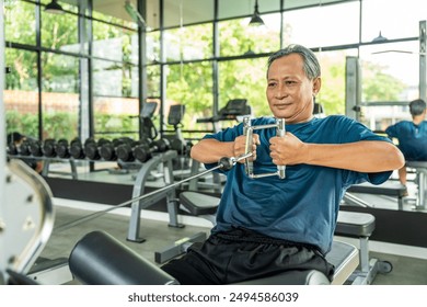 Old man weight training wearing sportswear. Asian mature exercise indoor gym. Bodybuilder good health. Fitness elderly pull up the machine bar in gym. - Powered by Shutterstock