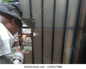 Old Man Welding A Corrosive Black Iron Handle Of Gate
