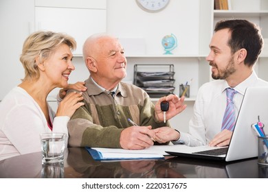 Old Man And And Woman Signing Car Sale Contract At Office And Hand Over Keys To Manager