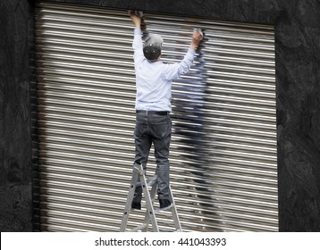  old  man working cleaning metal shutter door  without safety equipment  in  danger   in  metal ladder