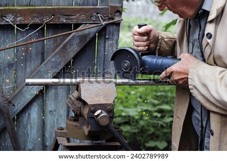 old man working. Cutting a metal pipe. spark. the pipe is clamped in a vice. man's hands hold a grinder. old iron vise, rusty pipe. electric tool, working with metal. Bulgarian, disc grinder