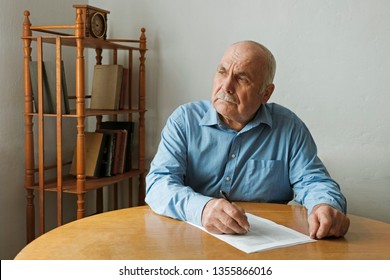 Old man writing notes or deciding whether to sign a paper document on the table in front of him as he looks to the side with a thoughtful engrossed expression