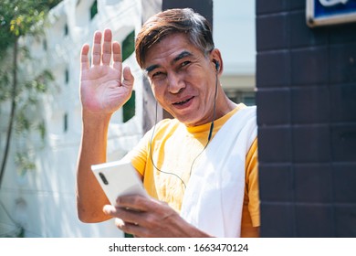 Old Man In Yellow T-shirt Standing In Front Of His House And Wave His Hand To Greeting The Neighbor.