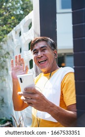 Old Man In Yellow T-shirt Standing In Front Of His House And Wave His Hand To Greeting The Neighbor.