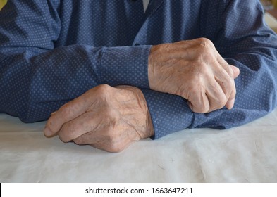 old man's hands on top of each other, in a blue shirt with white polka dots and black buttons