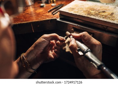 An old man's hands polish a piece of silver in a jewelry shop.The drill polishes the luxurious piece on the workbench with sandpaper. - Powered by Shutterstock