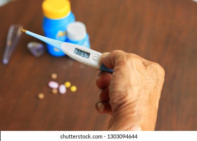 Old Man's Health Check His Temperature  At Home With Digital Thermometer.Found High Body Temperature.Some Medication On Table,take For Decrease Fever.Self Monitoring.Health And Medical Concept.