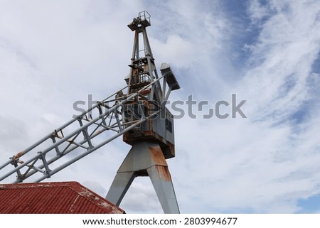 old maritime dockside crane, rust on metal components, latticed girder gib. swirling white clouds (close-up, marine, pier, waterfront)