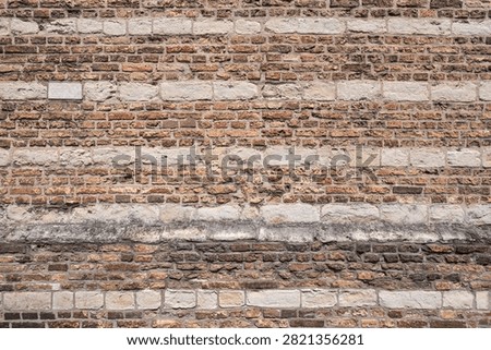 old masonry wall featuring alternating horizontal bands of reddish-brown clay bricks and lighter-colored ashlar stone blocks