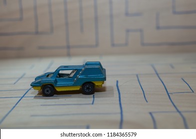 An Old Match Box Toy Car Running On A Wooden Labyrinth Pattern, Designed With A Blue Pen