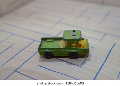 An Old Match Box Toy Car Running On A Wooden Labyrinth Pattern, Designed With A Blue Pen