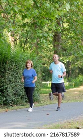 Old Mature Couple Of Man And Woman Running Together In The City Park To Be Fit And Healthy