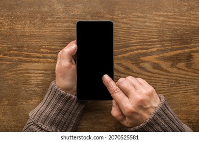 Old Mature Female Hands Holding Smartphone And Touching Black Screen With Finger On Brown Wooden Table Background. Senior Woman Using Modern Device. Closeup. Point Of View Shot. Empty Place For Text.