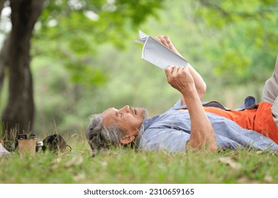 old mature male relax outside in nature garden,happy senior man smile,casual lying on his back on grass reading a book under a tree outdoor in the summer park,concept elderly people lifestyle,resting - Powered by Shutterstock