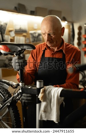 Old mechanic repairing a bicycle in the garage installing a new saddle. Copy space