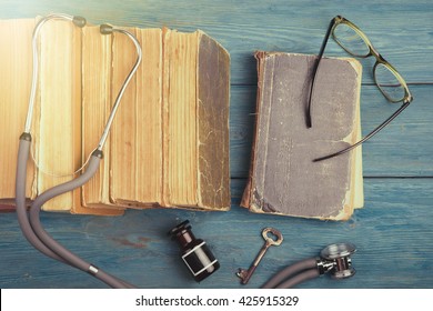 Old Medical Books With Stethoscope, Glasses, Bottle And Key On Blue Wooden Background