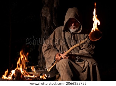 Old medieval monk by the fire with torch 