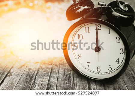 old memory time concept, retro clock timed at 12 o'clock on wood with sun light.