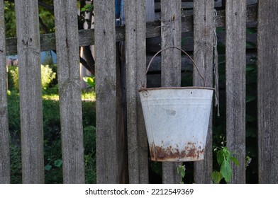 An Old, Metal Bucket Hangs On The Fence.