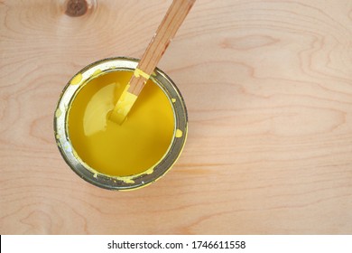Old metal can with yellow paint on light brown wooden background. Mixing white paint, yellow color with stick. Painting boards, construction work and repairs in country. Space for text