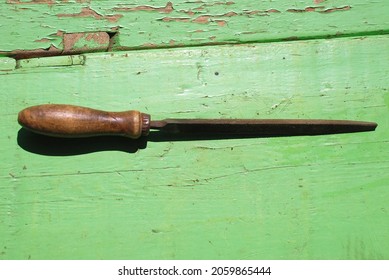 Old Metal File. A Medium Sized Triangular File With A Wooden Handle Lies On A Green Wooden Surface. Vintage Tool For Working On Metal And Wood.