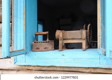 An old metal heavy iron with a wooden handle and a vintage dryer for things standing on the window sill of the old hut