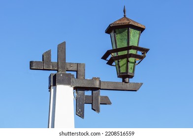 An Old Metal Outdoor Lantern On A Cement Pole Against A Blue Sky Background