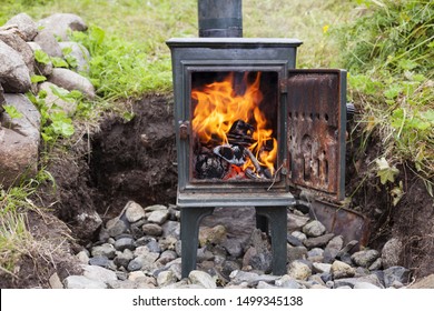 Old Metal Stove Outside. Scandinavian Style Wood Burning Stove, Flames Inside, Standing In Garden. Outdoor Living Room Project. 