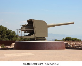 Old Military Cannon At Montjuïc Castle In Barcelona Spain Pointing To The Right. Clear Blue Sky With City In The Background.