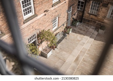 Old mill warehouse red brick courtyard with bench and trees on summer day. Looking out of old wooden sash window.
