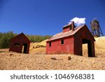 Old mining headframes in Cripple Creek Colorado. Red buildings with blue Skys and white clouds.