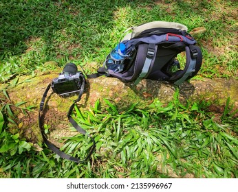An old mirrorless camera and hiking backpack laying on the ground with grass.