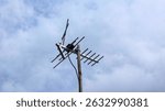 old model television (TV) antenna on top of house with cloudy blue sky background, analog antenna