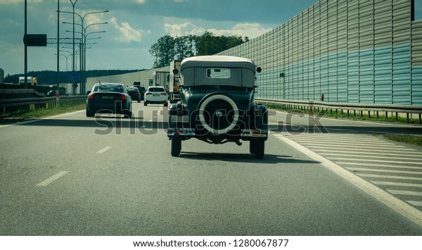 Old model vintage car driving on the highway with\
modern cars.