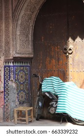 An old motorcycle covered in a striped cloth with a wooden stool in the archway of the ancient fortified wall of Marrakech, Morocco. - Shutterstock ID 663339232