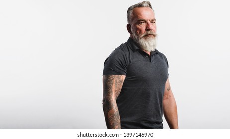 Old Muscular Man With A Short White Beard Looking At Camera. Portrait Of A Senior Man With Tattoo On Arms Isolated On White Background.