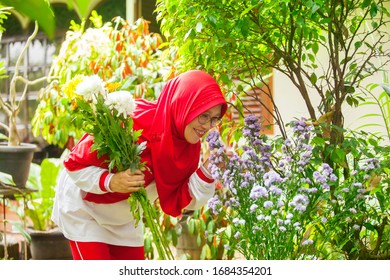 Old Muslim Woman Smelling Flowers While Holding Some Flowers At Home Backyard