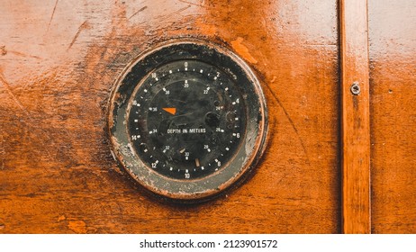 Old nautical depth meter on boat dashboard with worn wooden surface