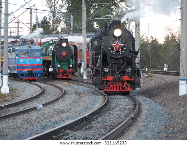 old and new: Russian steam train rides on the\
background of modern\
locomotives