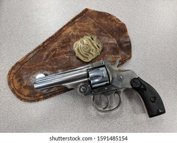 Old Nickel Plated Revolver With A Worn Brown Leather Holster And A Brass Deputy Sheriff Badge.